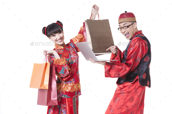 Excited young couple in Tang suit holding shopping bags and laptop