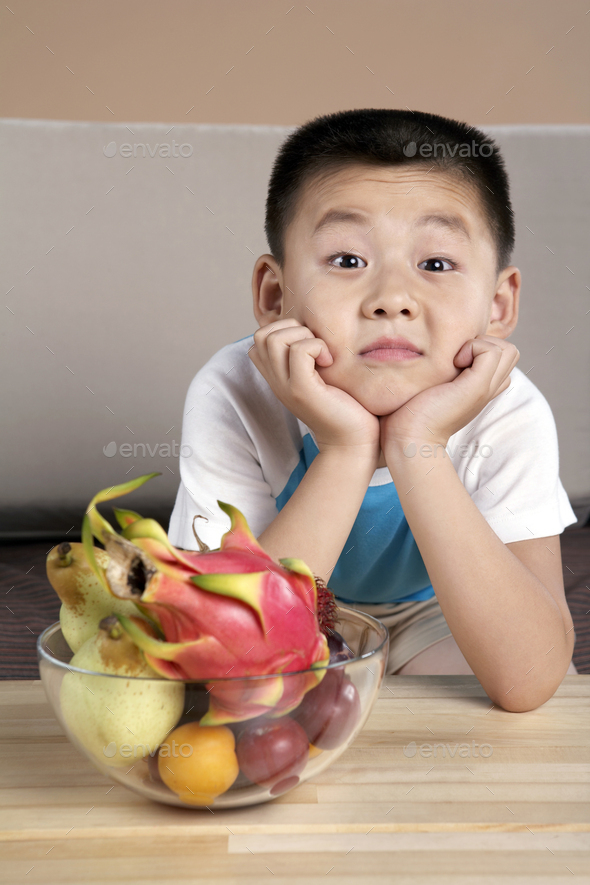 Chinese Elementary Aged Boy Leaning On A Table Next To A Bowl Of Fruit - Stock Photo - Images