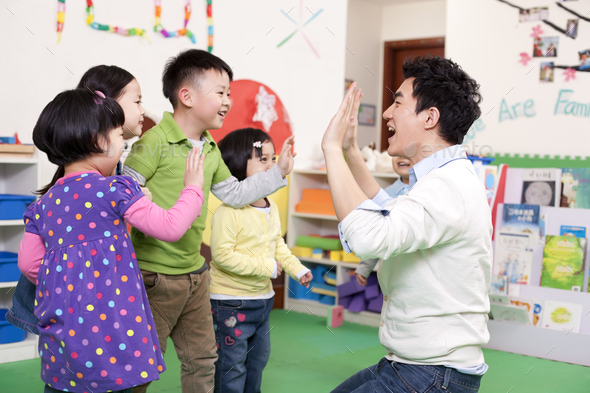 Happy kindergarten children playing clapping game with teacher