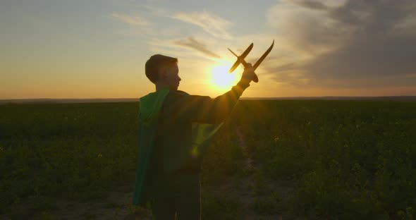 A Boy Is Standing on the Field and Playing with a Plane. Sunset.  alt