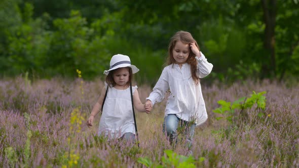 Happy little girls walking in a blooming sunny park.