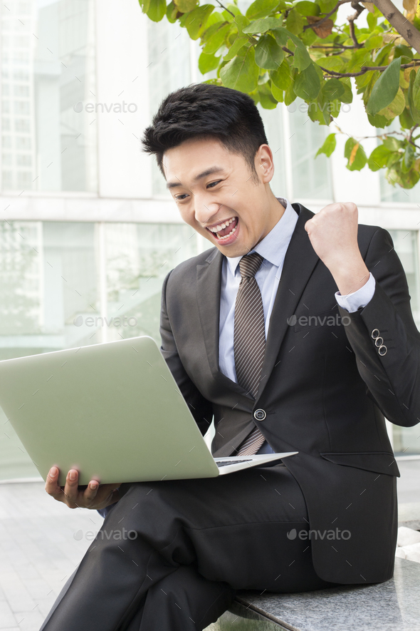 Young businessman with laptop punching the air with excitement outdoors