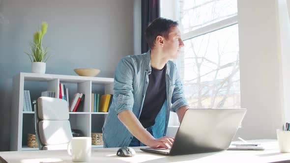 Young male entrepreneur works at home office at the computer. alt