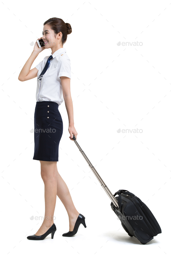Smiling airline stewardess with wheeled luggage making a phone call