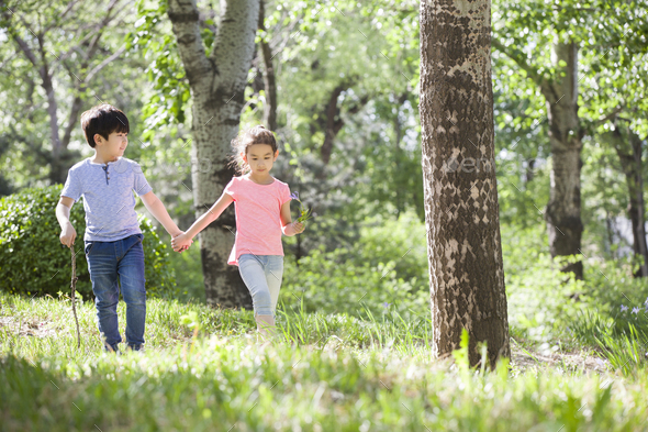 Happy children holding hands walking in woods Stock Photo by bluejeanimages