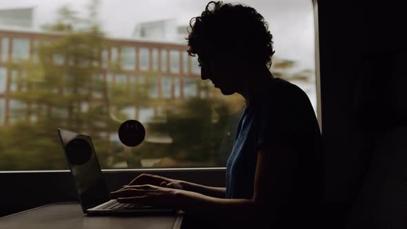 Silhouette of a Woman in Glasses Working on a Laptop While Going By Train alt