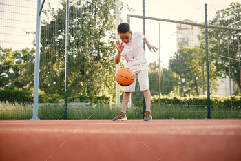Multiracial boy standing on a basketball court and play with an orange ball