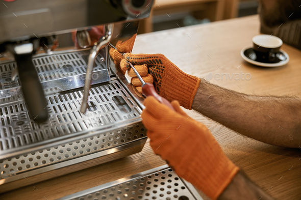 Male hands repairing coffee machine with screwdriver