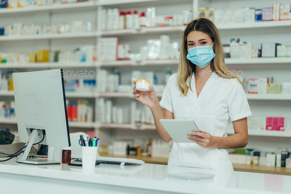 Pharmacist wearing protective mask and holding medical cream and a digital tablet