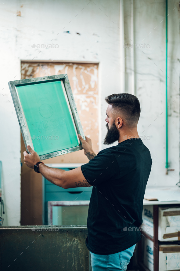 Male worker holds the silkscreen frame in a printing workshop