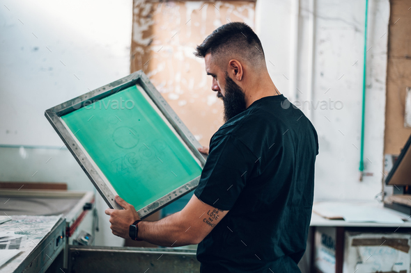 Male worker holds the silkscreen frame in a printing workshop