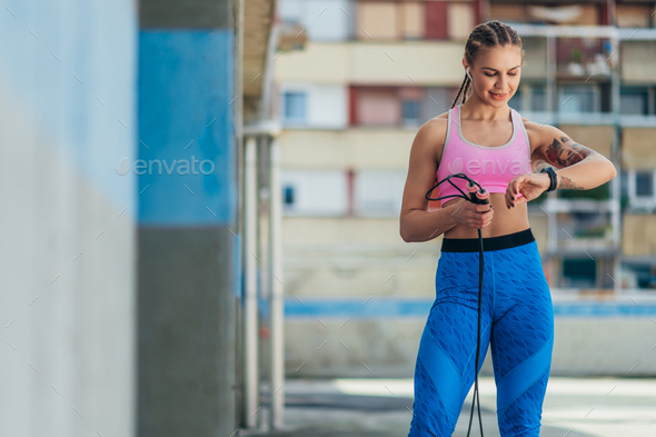 Attractive young woman using smartwatch and a fitness jump rope while training outside