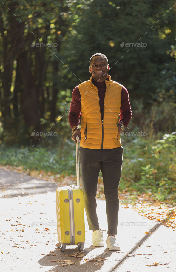 african american young man in stylish clothes with suitcase walks in an autumn park - Stock Photo - Images