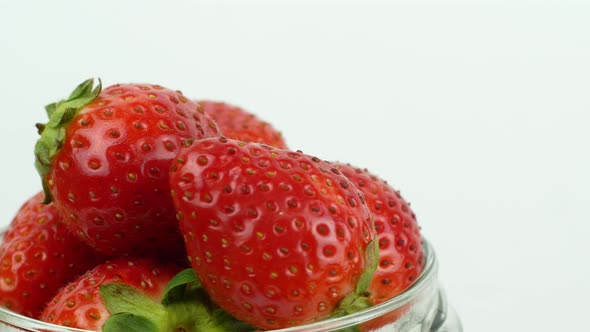 Glass jar with red ripe strawberries rotating counterclockwise on a white background.