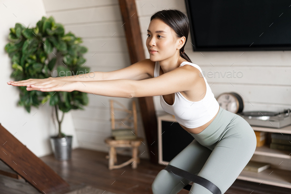 Cute Asian Fitness Girl At Home Doing Workout Squats With Stretching Elastic Rope On Her Legs