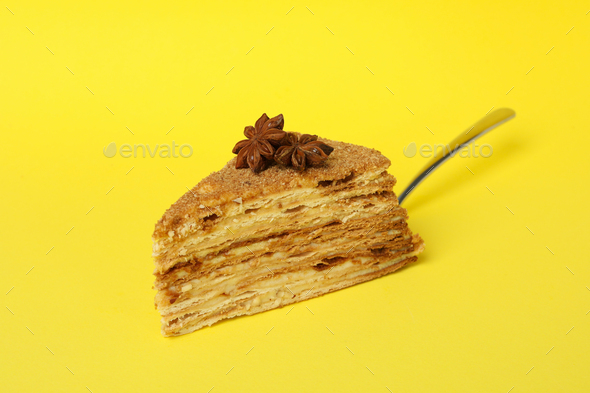 Spatula with piece of honey cake on yellow background