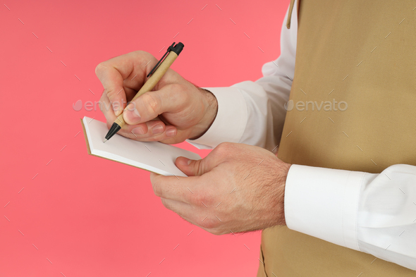 Waiter man write order in notebook on pink background