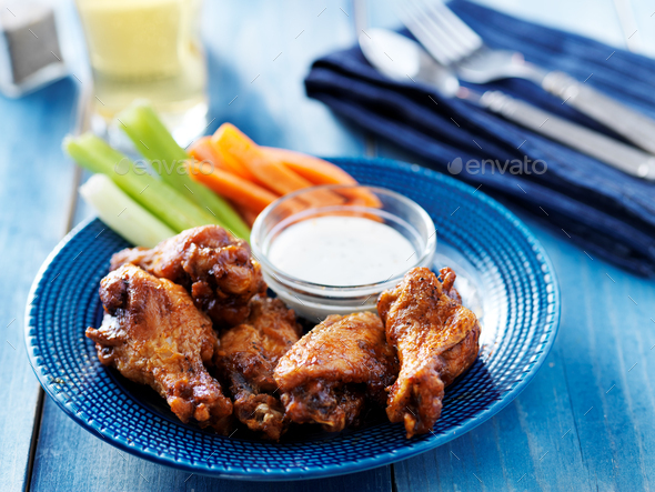 bbq buffalo chicken wings on blue plate with ranch dip and celery sticks