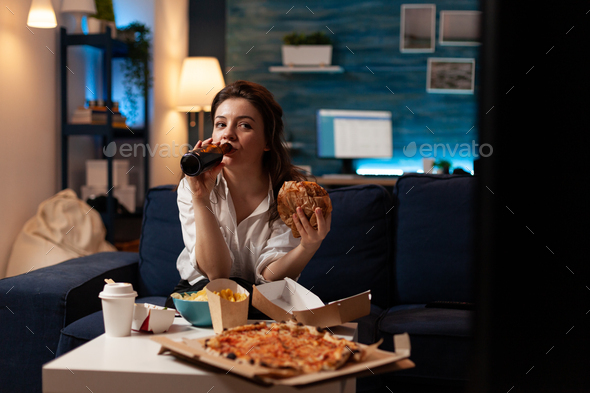 Happy woman drinking beer eating tasty delicious burger watching documentary series movie
