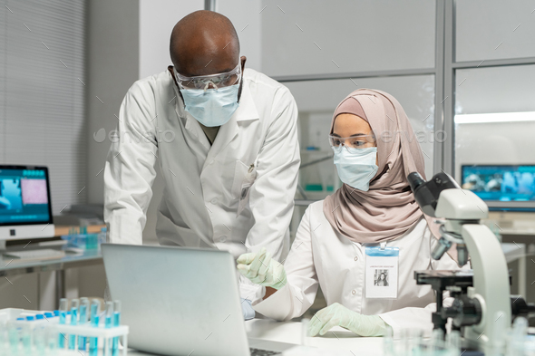 Young Muslim female virologist making presentation to African American colleague