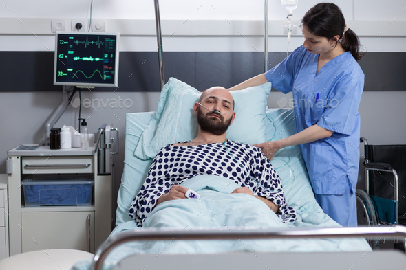 Nurse fixing pillow taking care of patient with respiratory insufficiency connected to vitals - Stock Photo - Images