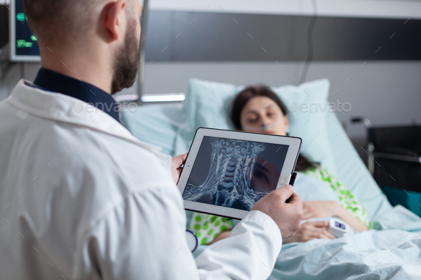 Medic holding digital tablet with throat mri looking at sleeping patient in hospital bed