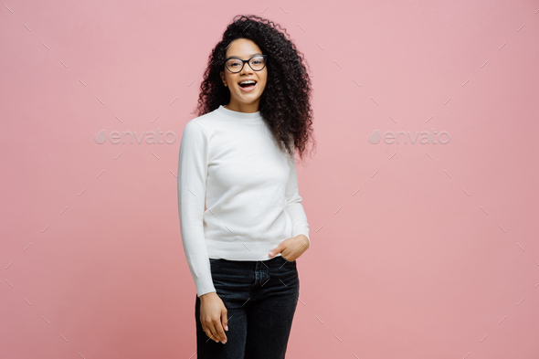 Cheerful woman going to work, laughs at something positive, wears neat white jumper and jeans