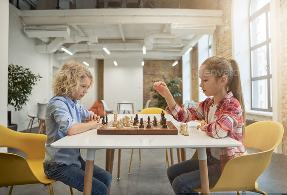 Two smart little children, boy and girl developing chess strategy, playing board game, sitting