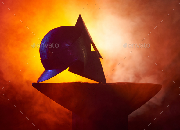 Gladiator helmet lying on anvil among fire and smoke