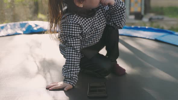Girl Looking at the Phone While Sitting on a Trampoline