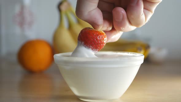 the Man Dips a Ripe Red Strawberry Into a Bowl of Whipped Cream with His Right Hand and Eats It