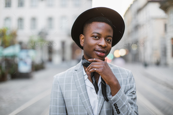African man in stylish wear and hat posing on city street