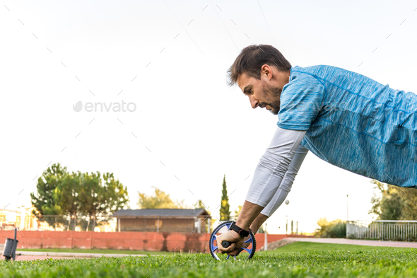 side view of caucasian bodybuilder with sportswear exercising with ab wheel on the grass