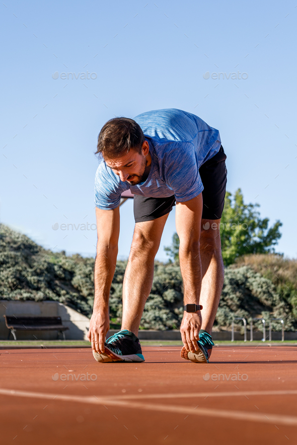 athletic young man stretching legs before running, warming up so as not to get injured