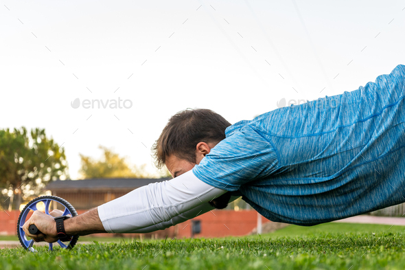 side view of unrecognizable caucasian with sportswear exercising with ab wheel on the grass