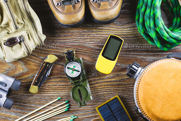 Hiking or travel equipment with boots, compass, binoculars, matches on wooden background