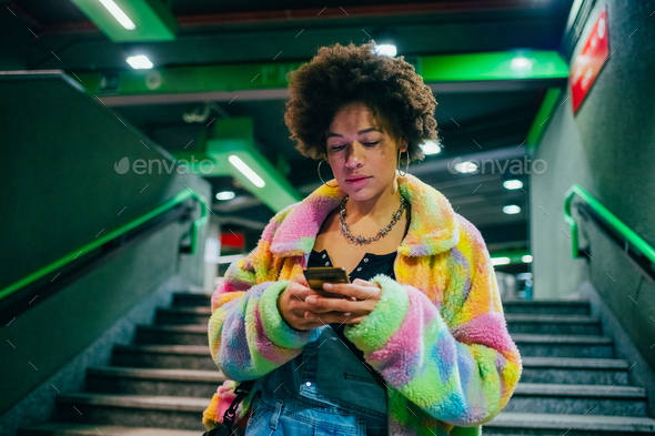 Young mixed race woman indoor metro station using smartphone