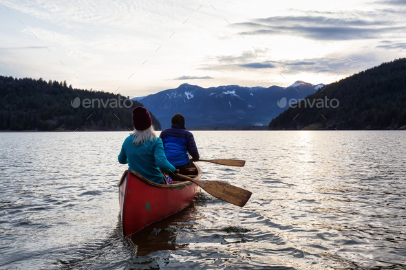 Adventurous people on a wooden canoe are enjoying the Canadian Mountain Landscape