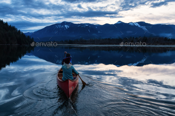 Adventurous people on a wooden canoe are enjoying the Canadian Mountain Landscape