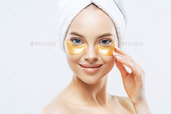 Happy tender woman applies golden patches under eyes, removes wrinkles and dark circles