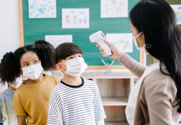Multi-ethnic group of children with face mask scan thermometer temperature in classroom
