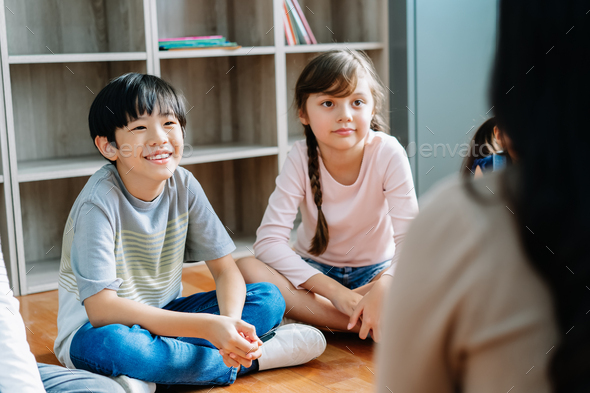 Elementary school kids sitting on the floor and looking at teacher in ...