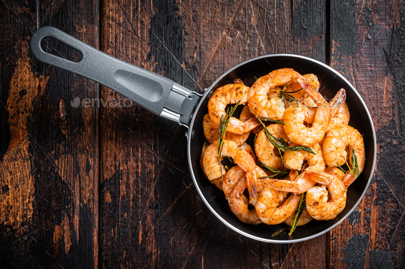 Fried with butter and garlic prawns shrimps in a skillet. Wooden background. Top view