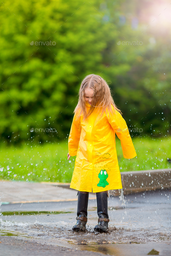 Little girl in raincoat and boots playing in the rain outdoors Stock Photo by travnikovstudio