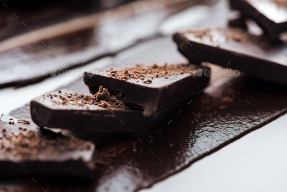 Selective focus of pieces of chocolate bar with cocoa powder and melted chocolate