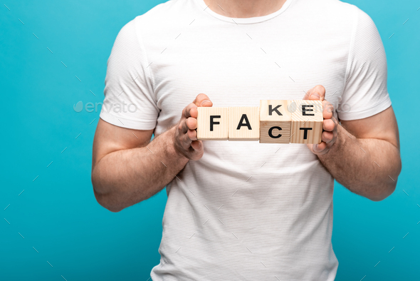 partial view of man in white t-shirt holding wooden cubes with fake fact lettering on blue