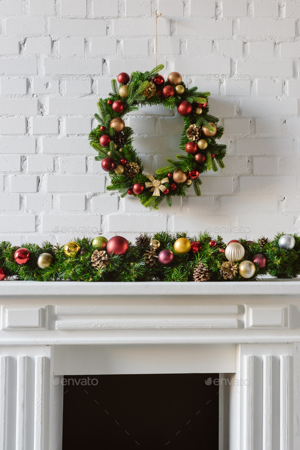 festive christmas wreath over fireplace mantel with white brick wall