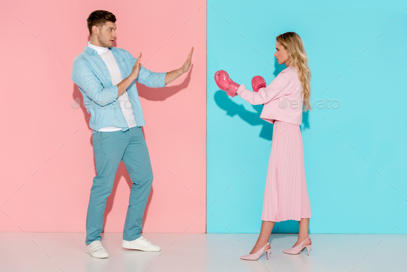 man gesturing with hands near aggressive woman in pink boxing gloves on pink and blue background