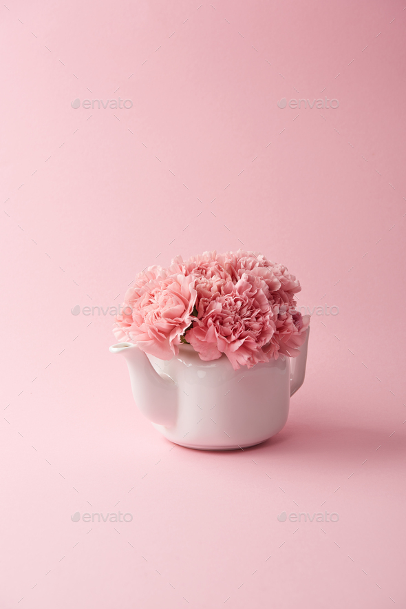 white kettle with beautiful tender pink flowers on pink background