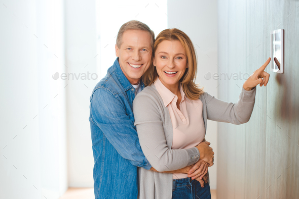 smiling husband hugging wife pointing at smart home control panel